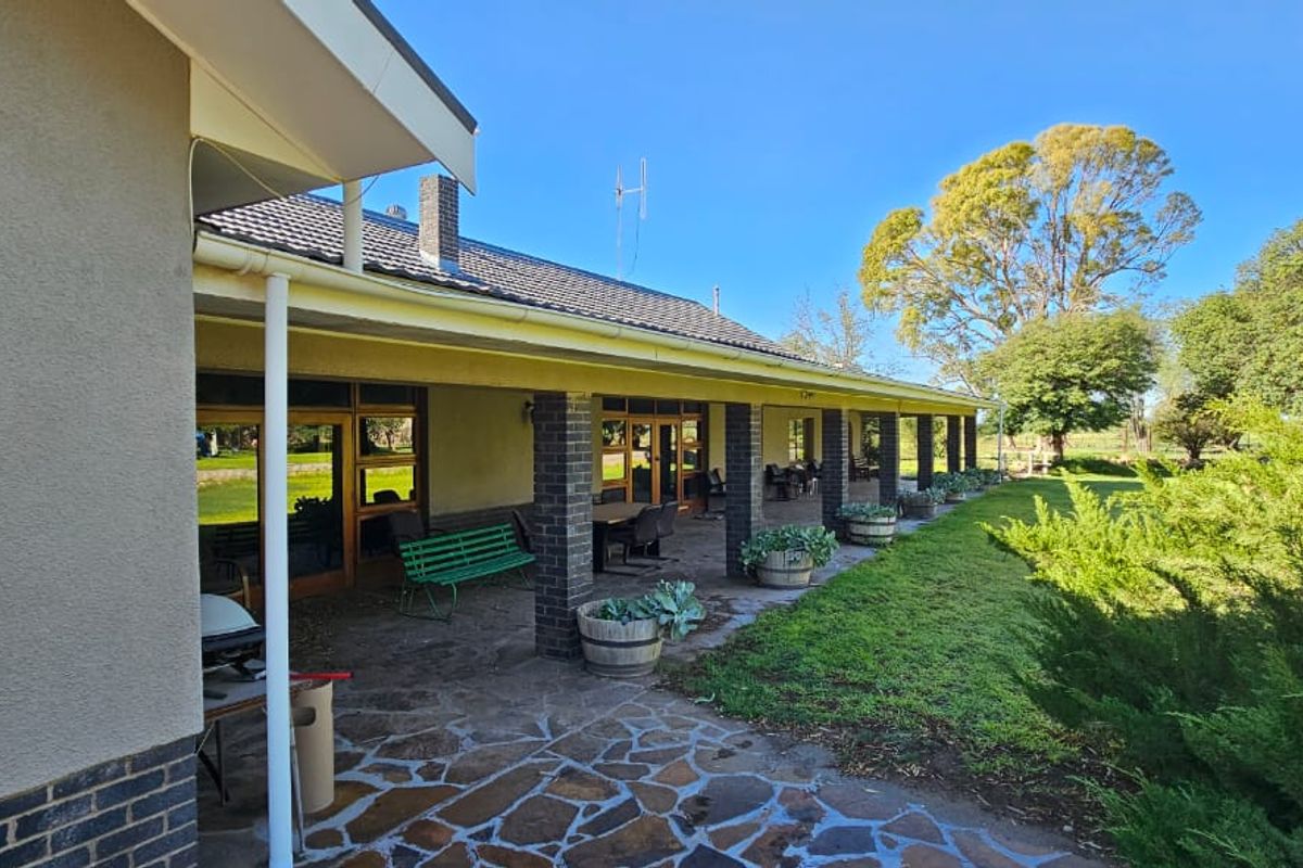 A spacious covered patio featuring stone paving, brick pillars, and direct access to the expansive garden and surrounding farm landscape.