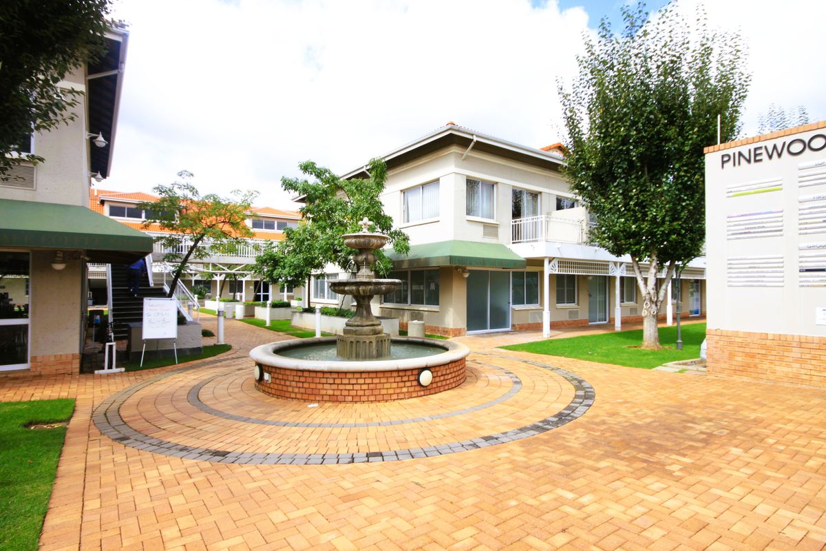 A well-maintained office park courtyard featuring a central stone fountain, brick paving, and landscaped greenery surrounded by multi-level office buildings.
