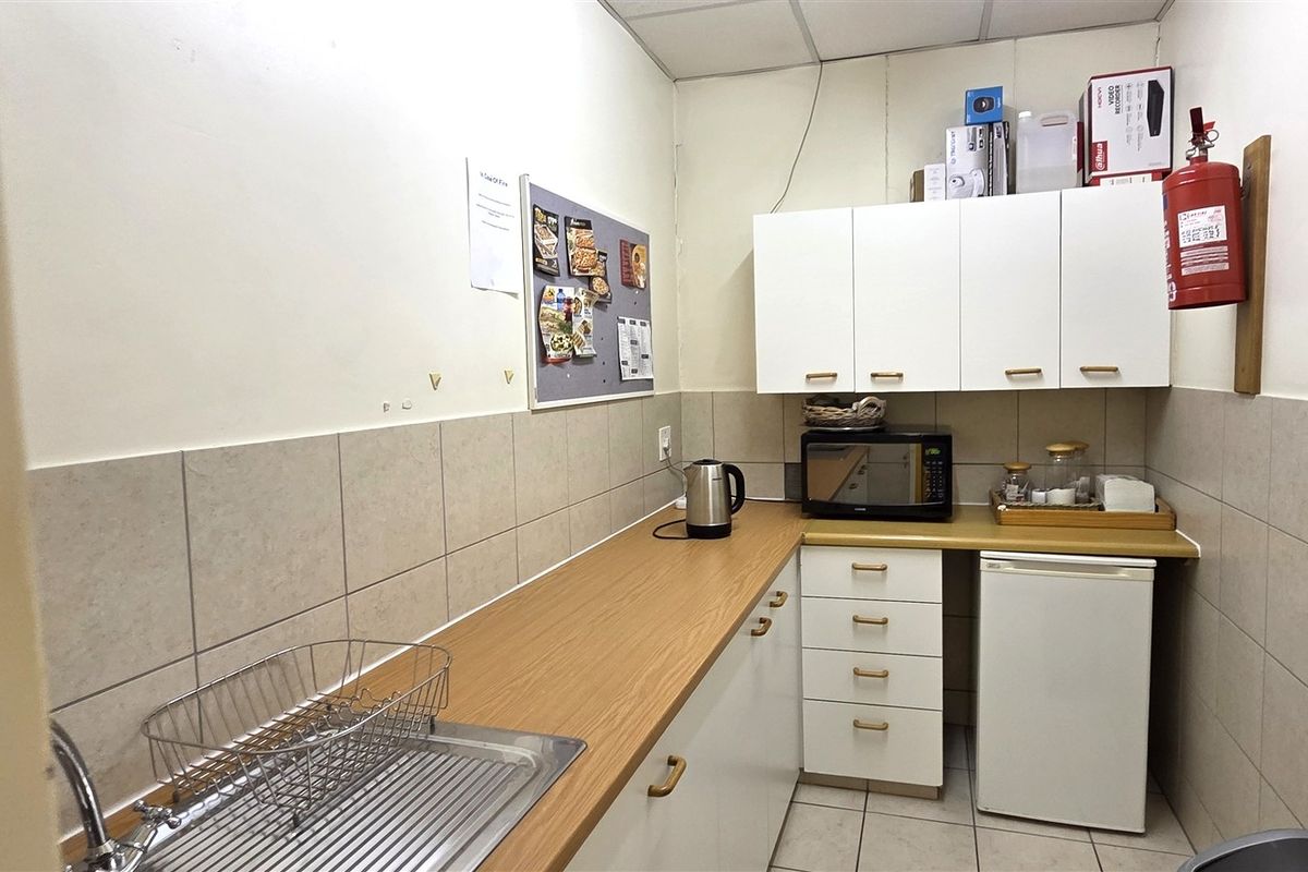 A compact office kitchenette featuring white cabinetry, laminate countertops, a stainless steel sink, and tiled backsplash, providing essential utility for the workspace.