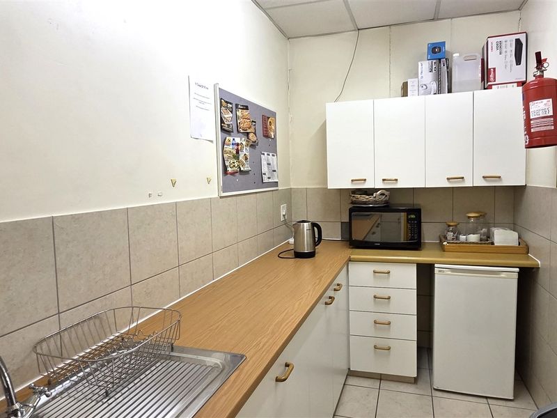 A compact office kitchenette featuring white cabinetry, laminate countertops, a stainless steel sink, and tiled backsplash, providing essential utility for the workspace.