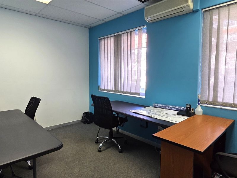 A functional office space featuring carpeted flooring, a suspended ceiling, split-system air conditioning, and large windows with vertical blinds.