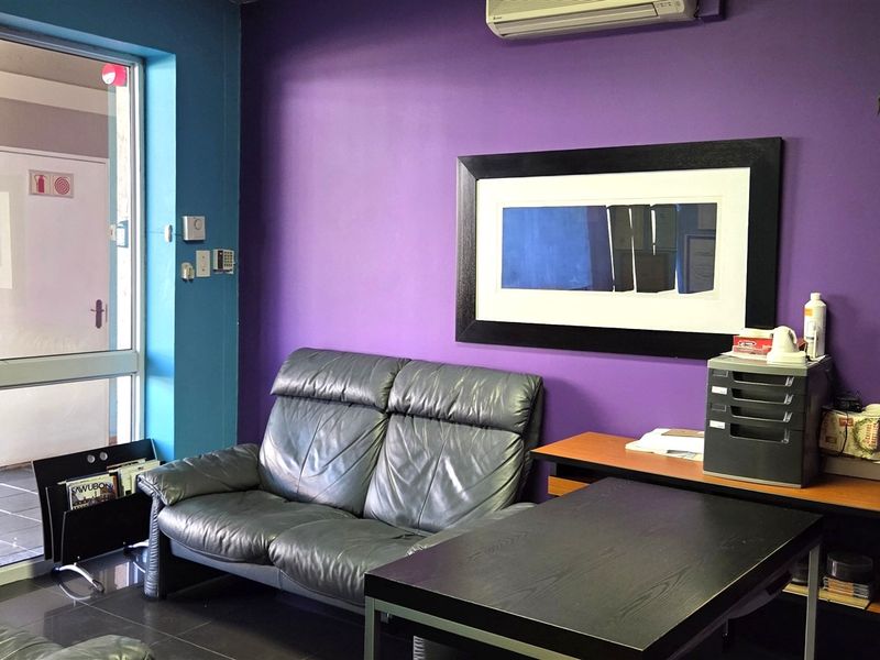 A functional office space featuring tiled flooring, a wall-mounted air conditioning unit, and a glass entrance door with access to an exterior walkway.