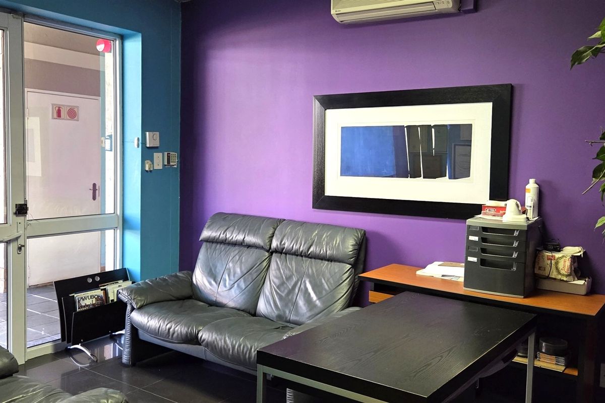A functional office space featuring tiled flooring, a wall-mounted air conditioning unit, and a glass entrance door with access to an exterior walkway.