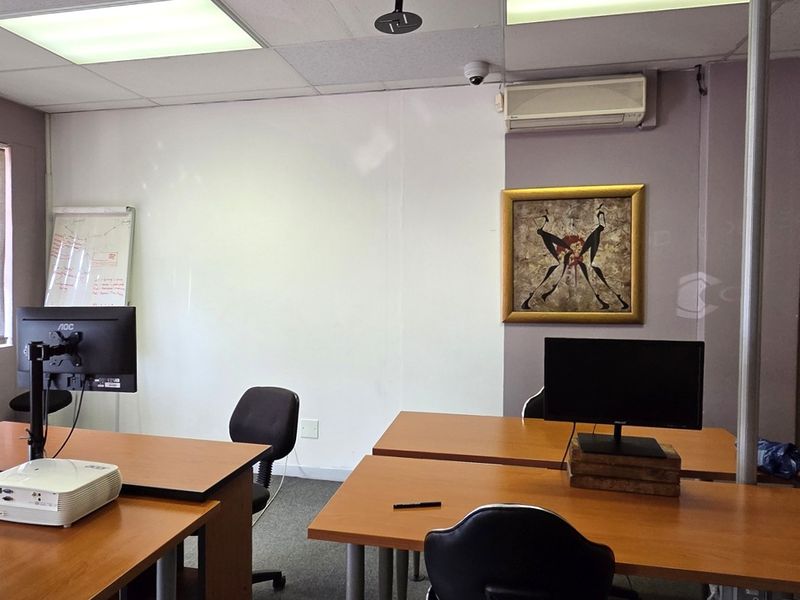 A functional office space featuring carpeted flooring, suspended ceiling with recessed lighting, vertical blinds, and a wall-mounted split-system air conditioning unit.