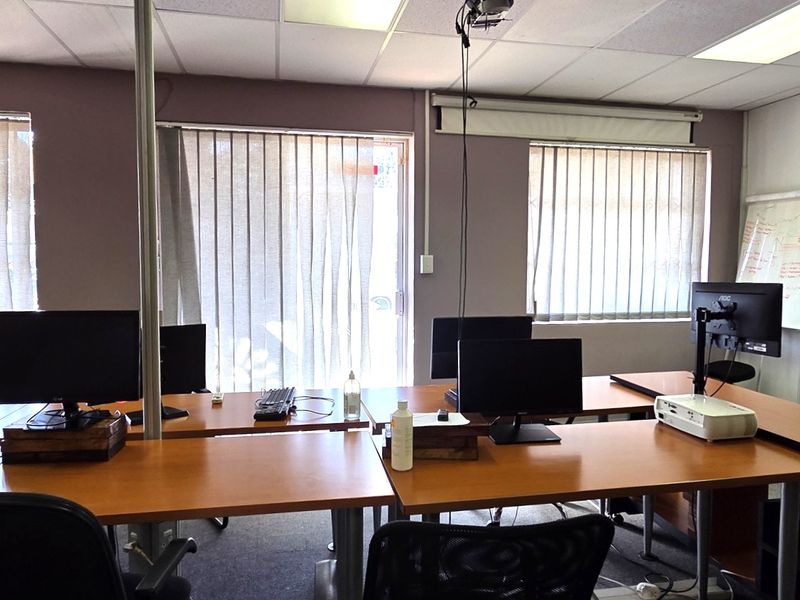 A functional office space featuring carpet flooring, suspended ceilings with recessed lighting, and multiple windows fitted with vertical blinds.