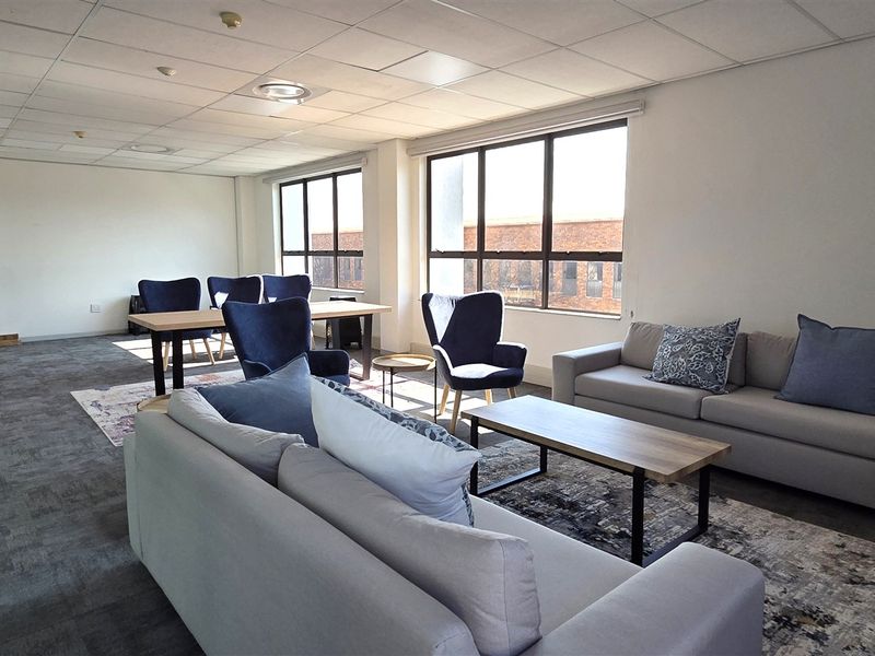 A spacious office area featuring a suspended ceiling, large windows providing natural light, and carpeted flooring, suitable for a professional workspace.