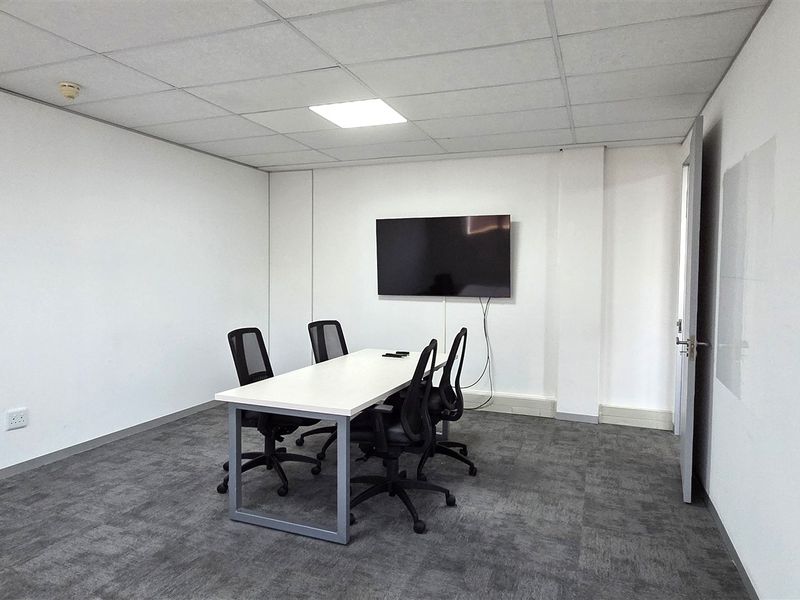 A functional office meeting room featuring a suspended ceiling, recessed lighting, and durable carpet tiles, equipped with a wall-mounted display screen.