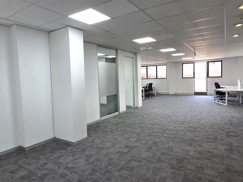 Spacious open-plan office area featuring modern carpet tiles, suspended ceilings with recessed lighting, and glass-partitioned meeting rooms.