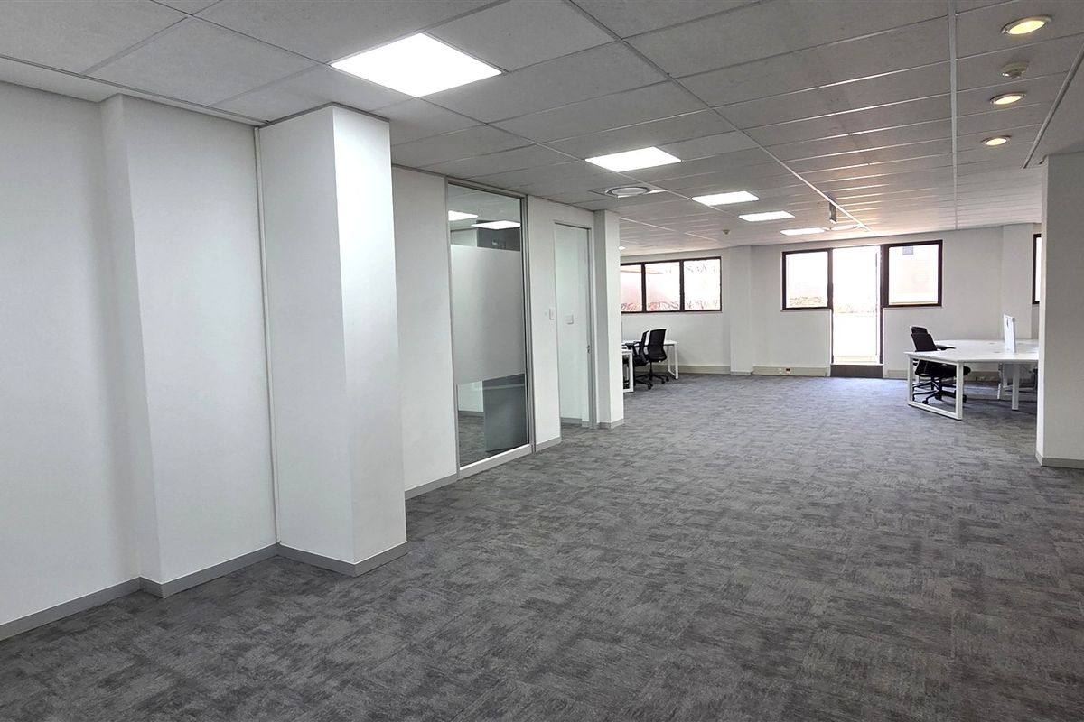 Spacious open-plan office area featuring modern carpet tiles, suspended ceilings with recessed lighting, and glass-partitioned meeting rooms.