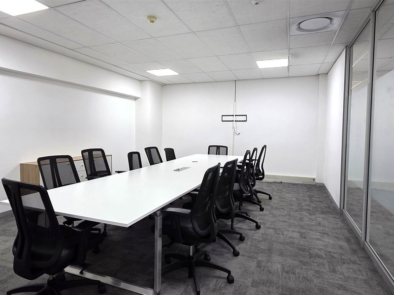 A professional boardroom or meeting room featuring a suspended ceiling, recessed lighting, carpeted flooring, and a glass partition wall.