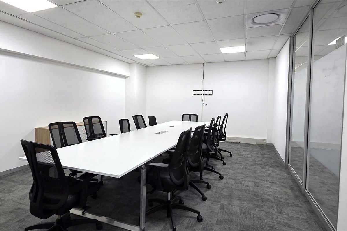 A professional boardroom or meeting room featuring a suspended ceiling, recessed lighting, carpeted flooring, and a glass partition wall.