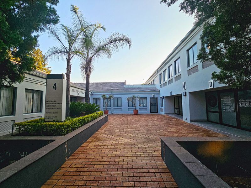 A well-maintained office park courtyard featuring brick paving, raised garden beds, and multiple designated office entrances with professional signage.