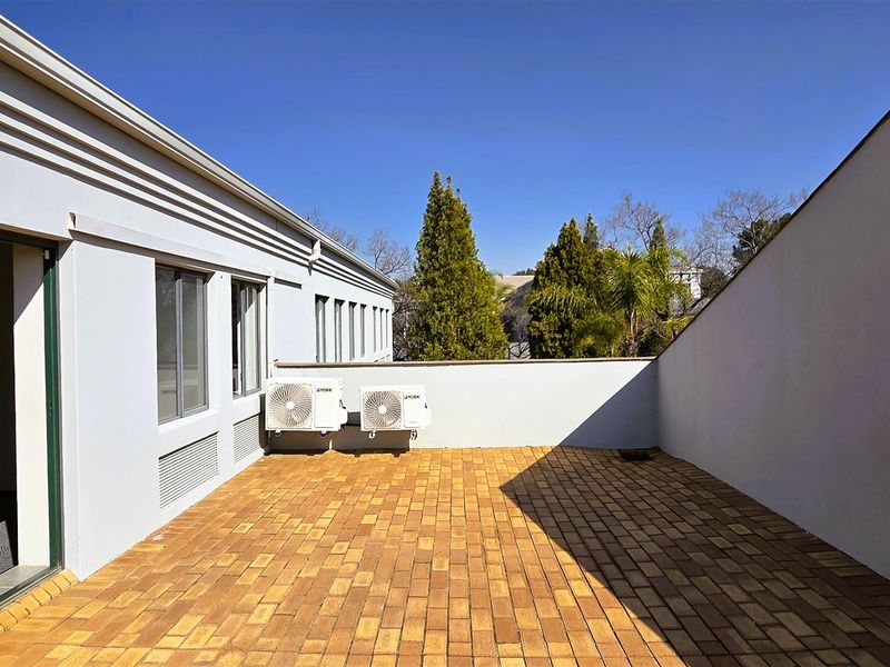 A spacious outdoor balcony featuring brick paving, sliding door access, and wall-mounted air conditioning units, offering a clean and functional exterior space.