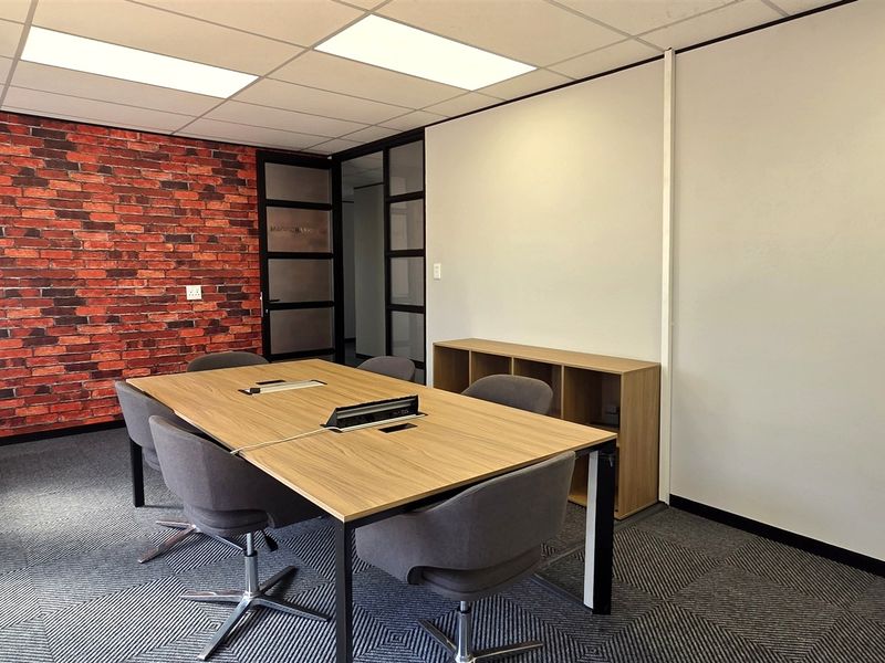 A modern office space featuring a brick accent wall, suspended ceiling with recessed lighting, and durable carpet tiles, providing a professional work environment.