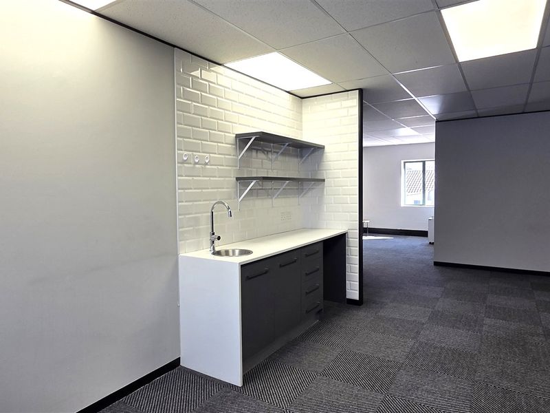 Modern office space featuring a clean kitchenette area with subway tile backsplash, drop ceiling, and professional carpet tile flooring.