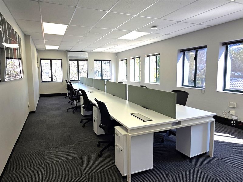 A well-lit, professional office space featuring suspended ceilings, recessed lighting, carpet tiles, and large windows providing ample natural light.