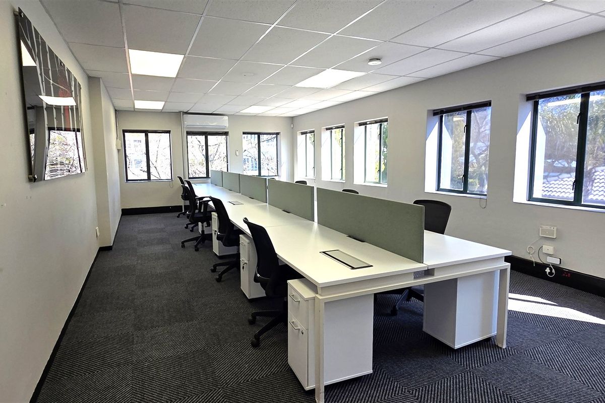 A well-lit, professional office space featuring suspended ceilings, recessed lighting, carpet tiles, and large windows providing ample natural light.