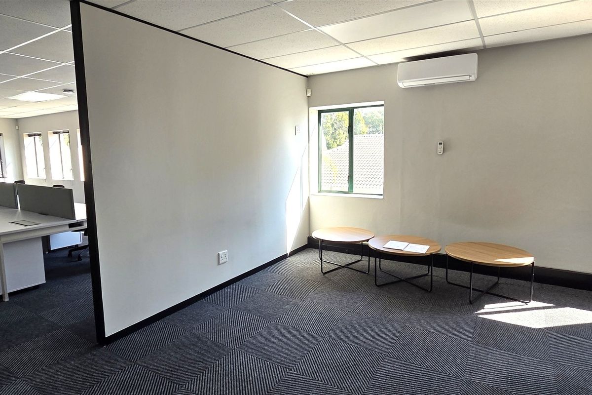 A bright, open-plan office space featuring carpeted flooring, a suspended ceiling, and a split-system air conditioning unit, providing a functional professional work environment.