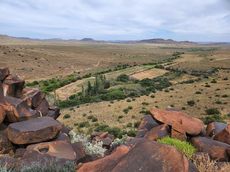 A panoramic view of the expansive farm landscape, featuring natural rock formations in the foreground and open grazing fields in the distance.