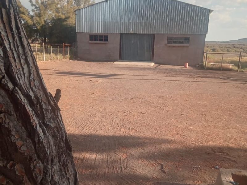 A detached farm shed or utility building featuring corrugated metal cladding and a large central entrance, situated on a spacious dirt yard.