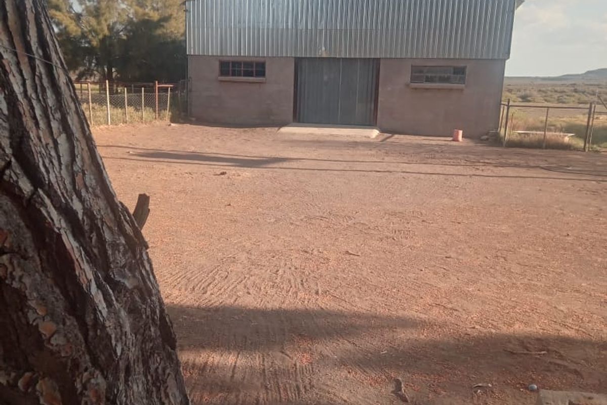 A detached farm shed or utility building featuring corrugated metal cladding and a large central entrance, situated on a spacious dirt yard.