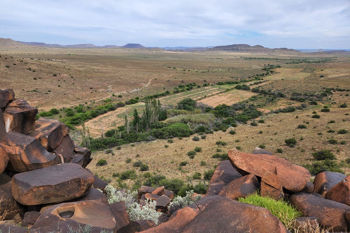 A panoramic view of the expansive farm landscape, featuring natural rock formations in the foreground and open grazing fields in the distance.