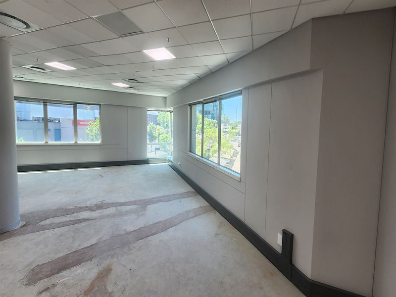 An empty, open-plan office space featuring a suspended ceiling, recessed lighting, and large windows providing ample natural light.