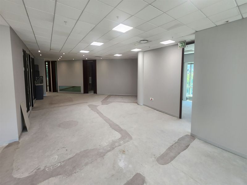 An open-plan office space featuring a suspended ceiling with recessed lighting and unfinished flooring, ready for final floor covering installation.