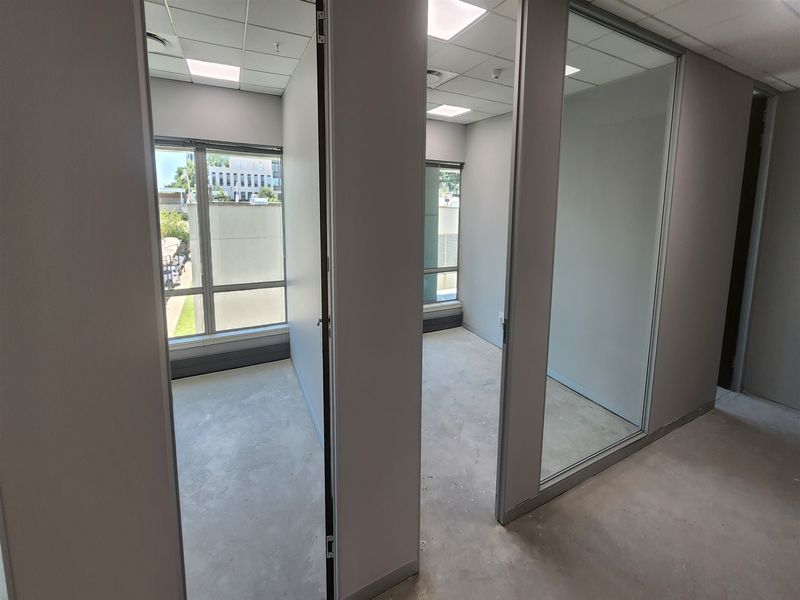 A series of vacant office spaces featuring glass partitions, suspended ceilings, and large windows providing natural light.