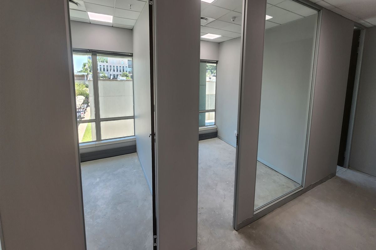 A series of vacant office spaces featuring glass partitions, suspended ceilings, and large windows providing natural light.