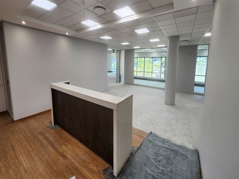 An open-plan office space featuring a built-in reception desk, suspended ceiling with recessed lighting, and large windows providing natural light.