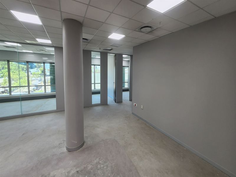 An open-plan office space featuring a suspended ceiling, recessed lighting, glass partitioning, and a structural column, currently awaiting final floor finishes.