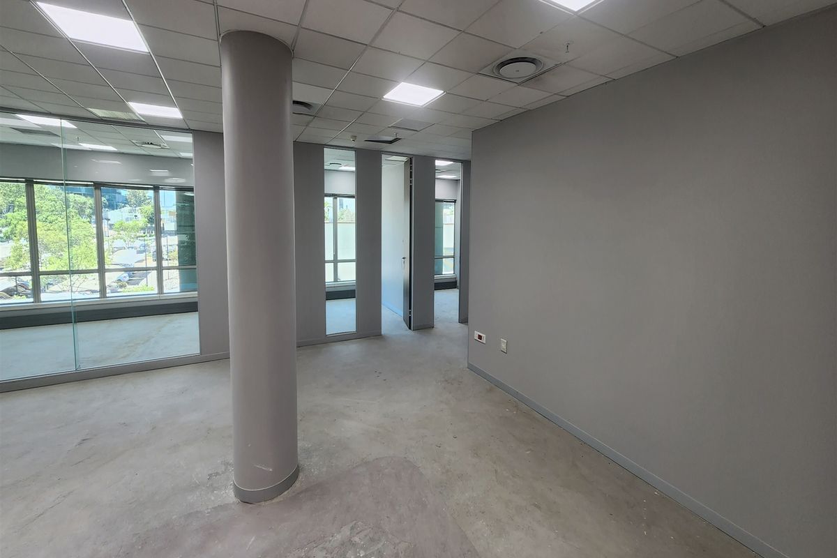 An open-plan office space featuring a suspended ceiling, recessed lighting, glass partitioning, and a structural column, currently awaiting final floor finishes.