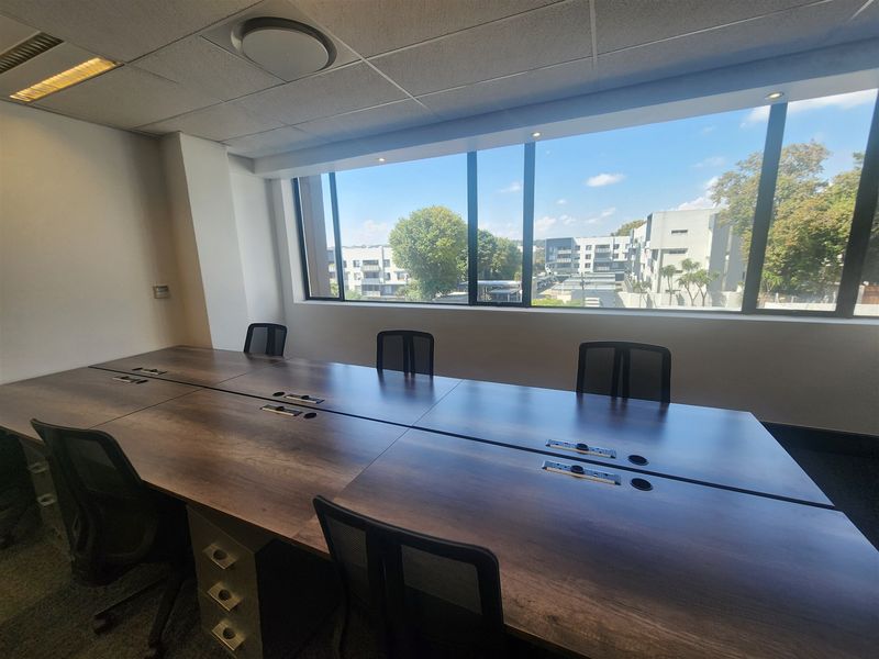A bright office space featuring a large window with neighborhood views, suspended ceiling, recessed lighting, and carpeted flooring.