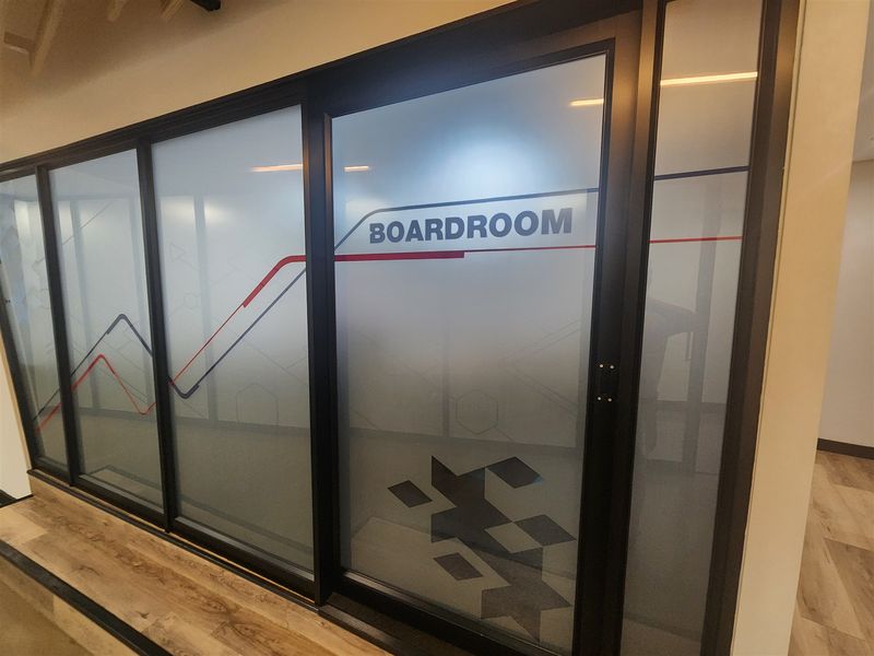 Modern office boardroom featuring a sleek black aluminum frame with frosted glass partitioning and durable laminate flooring.
