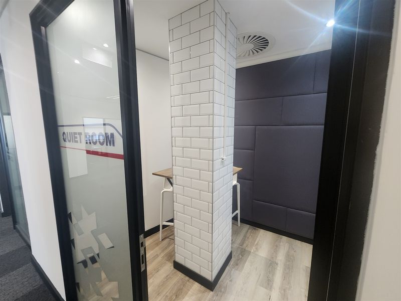 A modern, compact quiet room featuring a subway tile column, acoustic wall paneling, and a glass entry door, designed for focused work.
