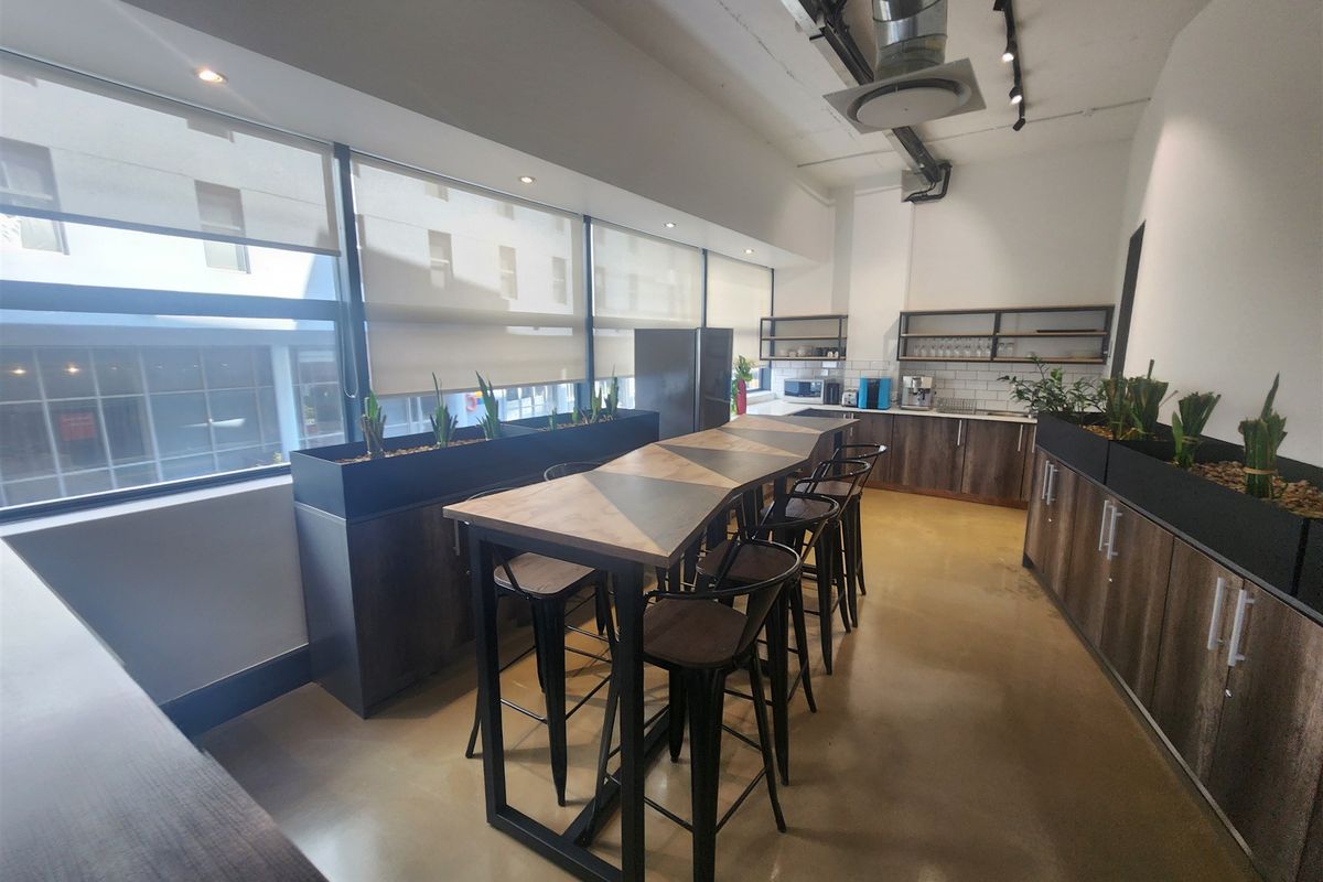 Modern office kitchen area featuring polished concrete floors, built-in cabinetry, subway tile backsplash, and industrial-style exposed ducting with integrated track lighting.
