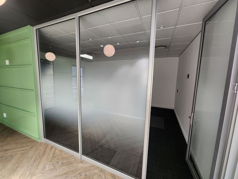 Modern office space featuring a glass partition wall, suspended ceiling, and stylish herringbone flooring, providing a clean and professional work environment.
