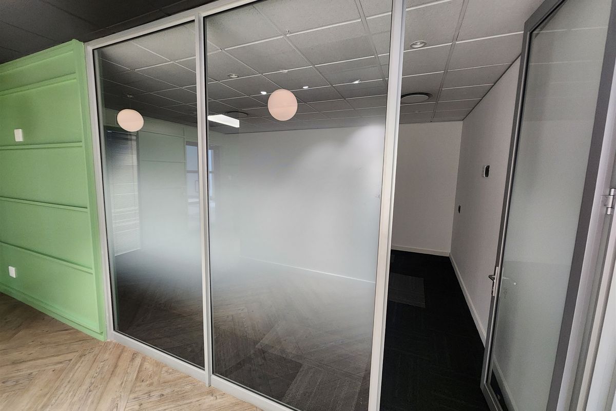Modern office space featuring a glass partition wall, suspended ceiling, and stylish herringbone flooring, providing a clean and professional work environment.