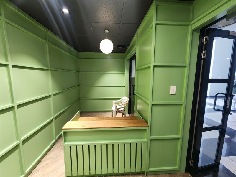 A compact office space featuring vibrant green wainscoting, a built-in reception desk, and modern lighting, providing a professional and distinct workspace environment.