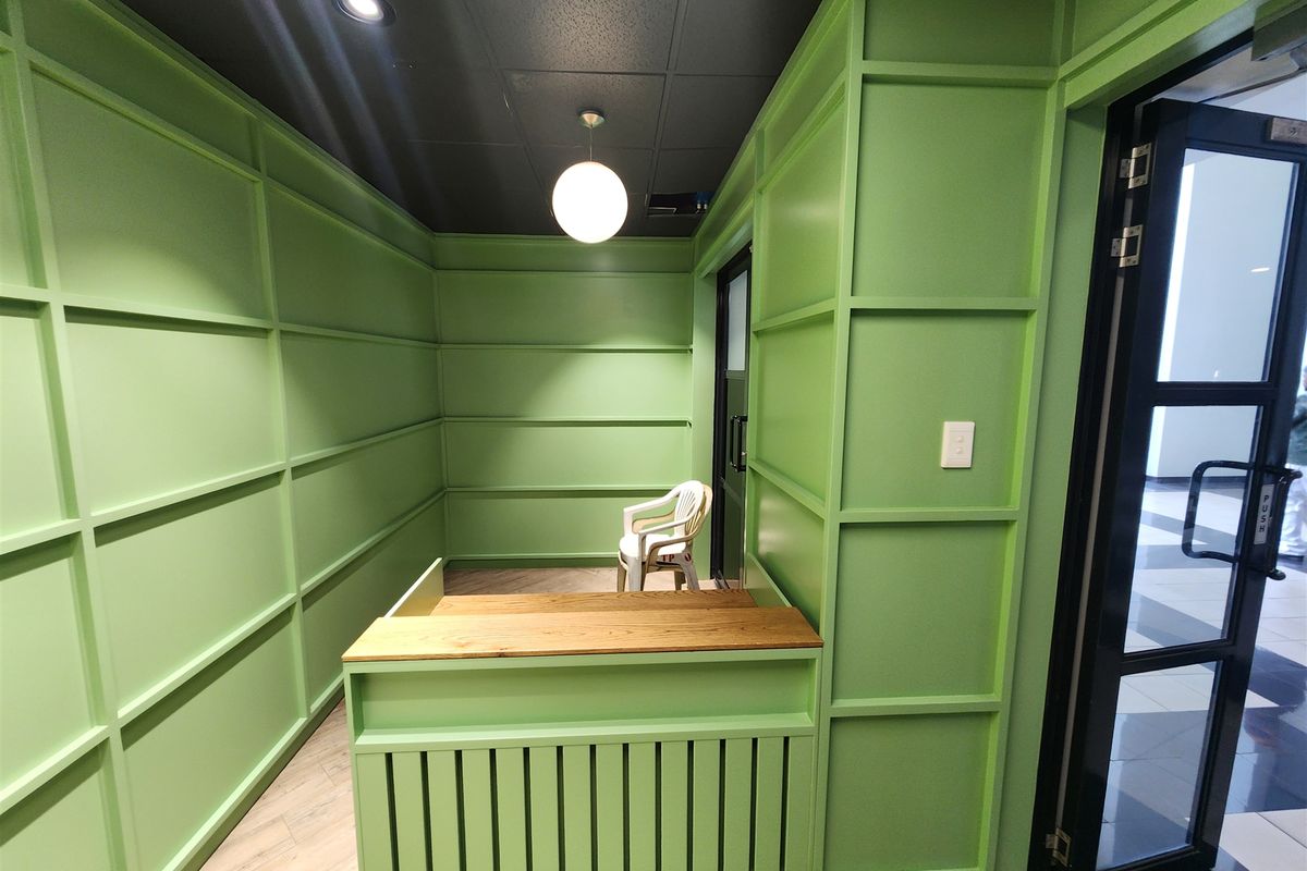 A compact office space featuring vibrant green wainscoting, a built-in reception desk, and modern lighting, providing a professional and distinct workspace environment.
