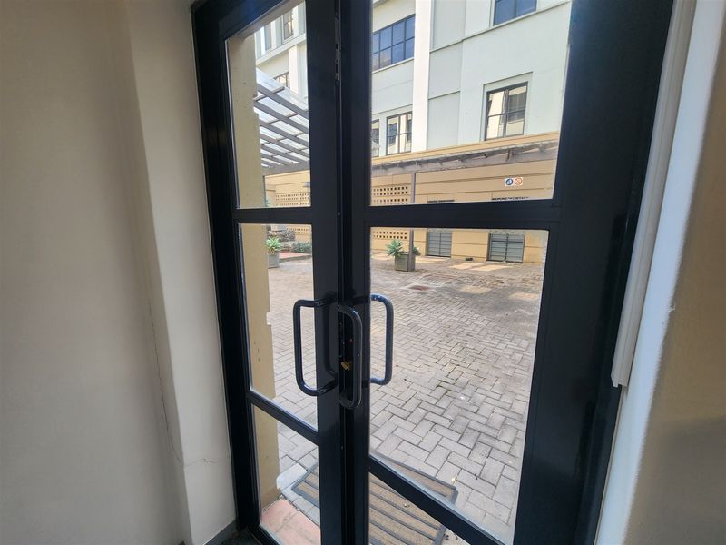 View from an interior entrance through double glass doors looking out onto a paved courtyard area with a metal pergola structure.