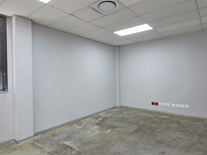 An empty office space featuring a suspended ceiling, recessed lighting, venetian blinds, and multiple electrical and data points, requiring new floor finishes.