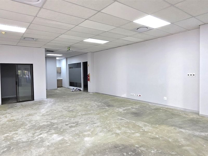 Spacious open-plan office area featuring a suspended ceiling, recessed lighting, and an unfinished concrete floor, ready for custom flooring installation.