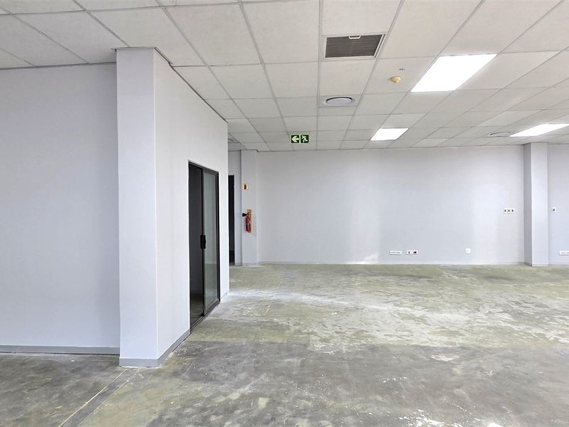 A spacious, open-plan office area featuring a suspended ceiling, recessed lighting, and unfinished concrete flooring, ready for custom fit-out.
