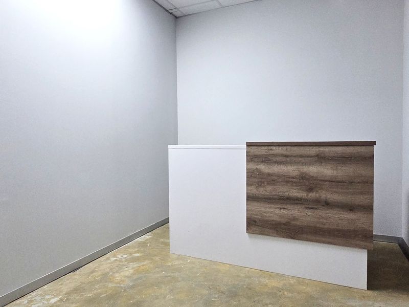 A minimalist office space featuring a built-in reception desk, neutral walls, and a glass entry door, ready for professional fit-out.