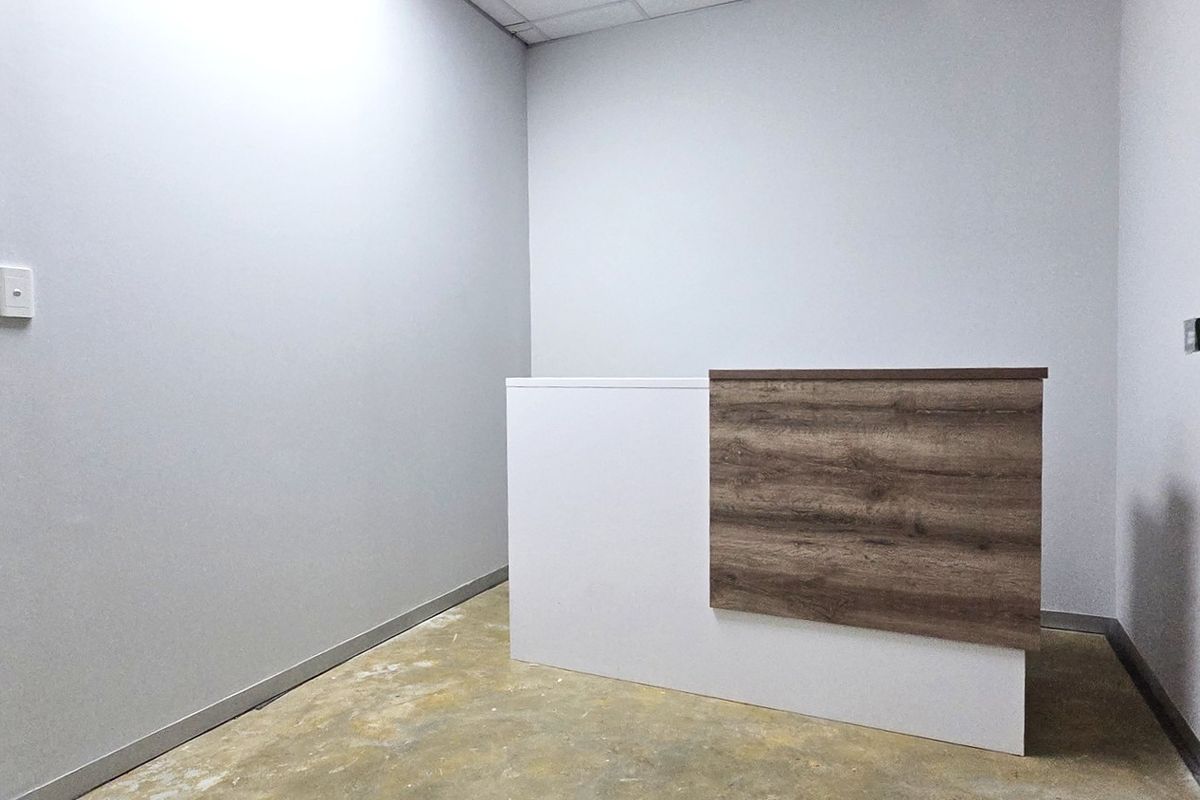 A minimalist office space featuring a built-in reception desk, neutral walls, and a glass entry door, ready for professional fit-out.
