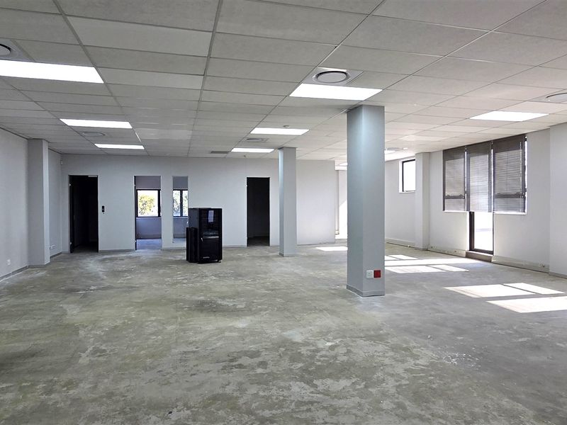 A spacious, open-plan office area featuring a suspended ceiling, recessed lighting, and large windows with blinds, currently awaiting floor finishes.