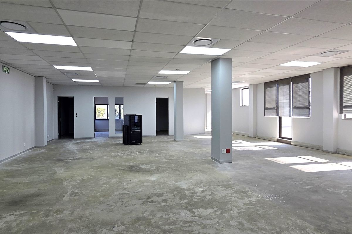 A spacious, open-plan office area featuring a suspended ceiling, recessed lighting, and large windows with blinds, currently awaiting floor finishes.