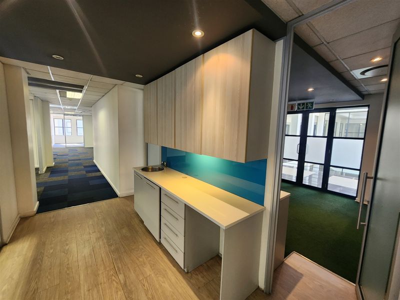 A modern office kitchenette featuring built-in cabinetry, a laminate countertop with a stainless steel sink, and a vibrant blue glass splashback.
